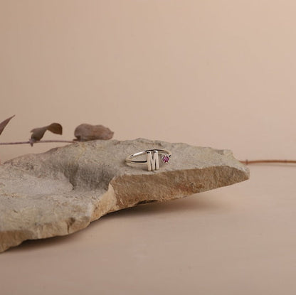 Silver ring with a red gemstone on a textured stone surface against a beige background