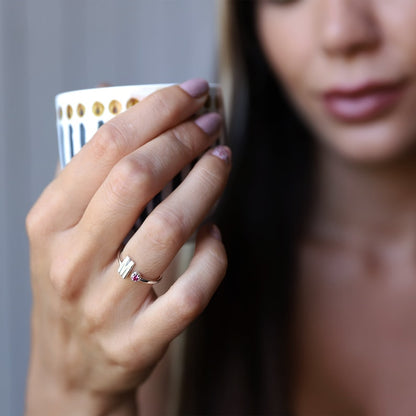 Close-up of a hand with an initial and gemstone ring holding a mug.