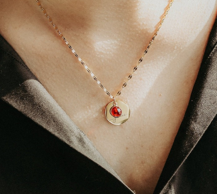 Necklace with a red gemstone pendant on a person's neck against a black background