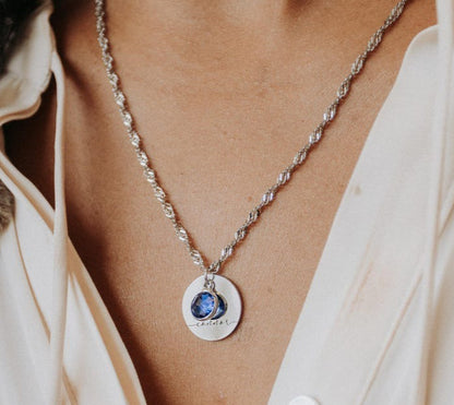 Necklace with a round pendant featuring a blue gemstone worn by a person in a light-colored shirt.