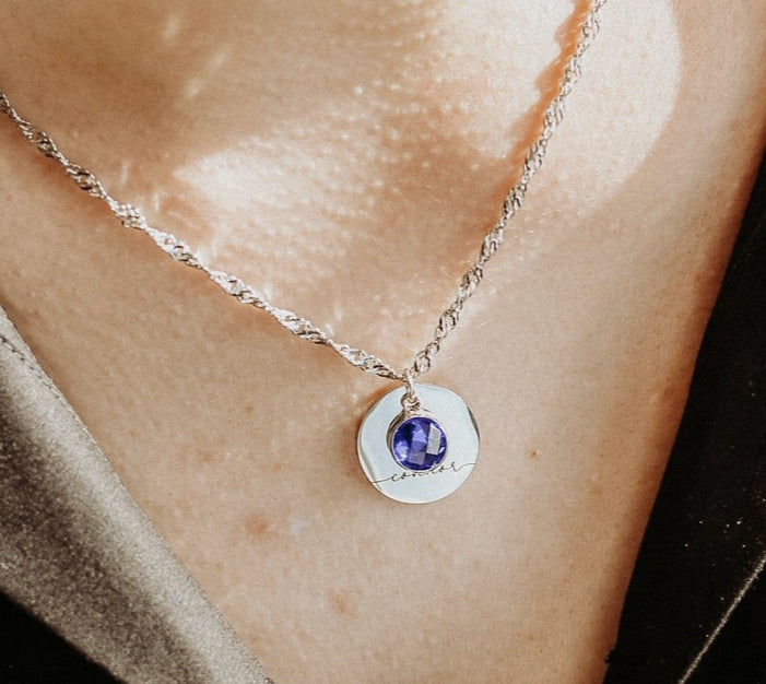Necklace with a pendant featuring a purple gemstone on a person's neck.