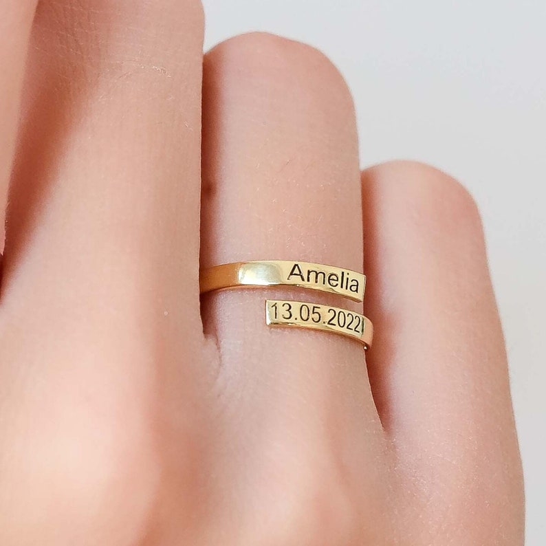 Gold ring with 'Amelia' and '13.05.2022' engraved on a finger against a neutral background