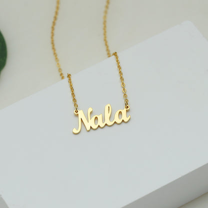 A gold-coloured name necklace with the name 'Nala' written in cursive script on a white surface.