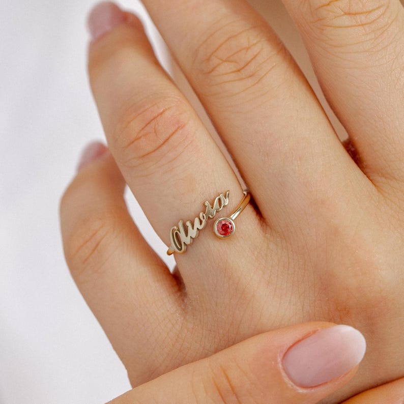 Gold ring with 'Olivia' and a red gemstone on a hand against a white background