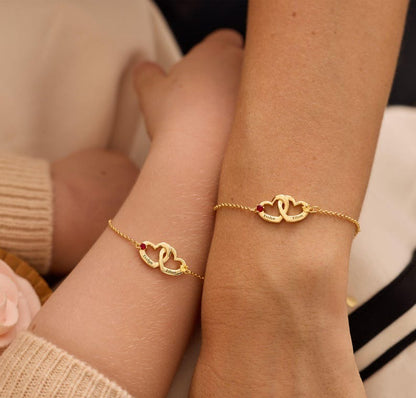 Two gold bracelets with heart designs on wrists against a neutral background