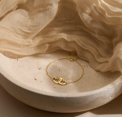 Gold bracelet with a heart design and chain on a beige fabric background