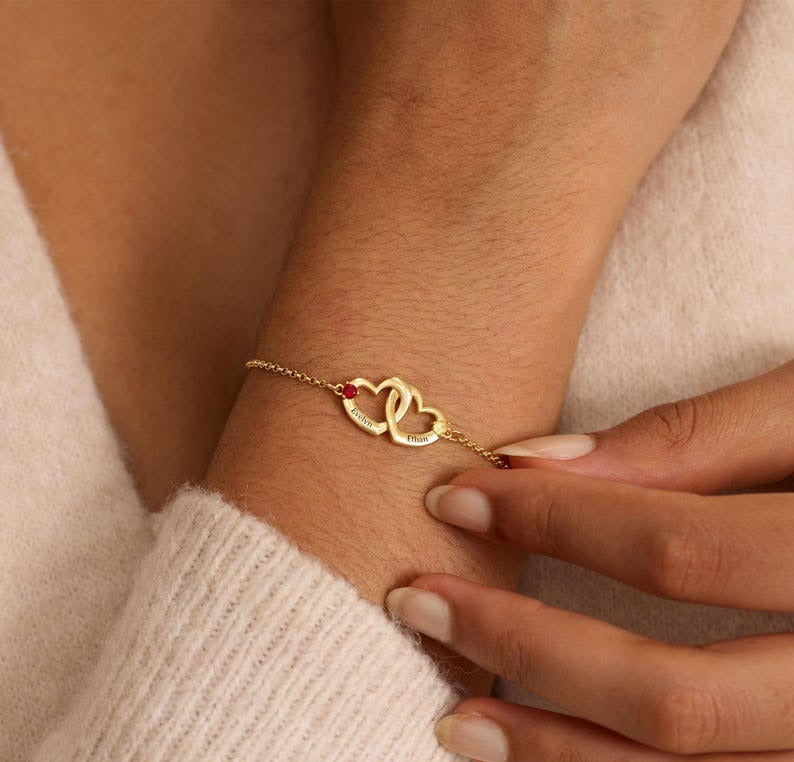 Gold bracelet with heart symbols on a wrist against a beige background