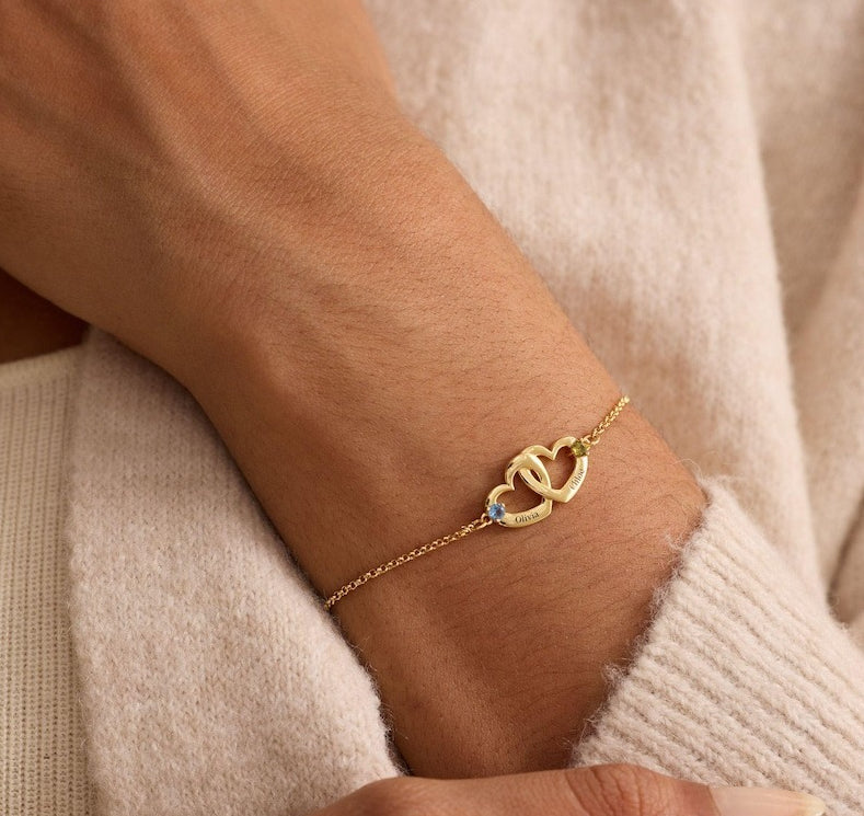 Gold bracelet with heart design on a wrist against a beige background