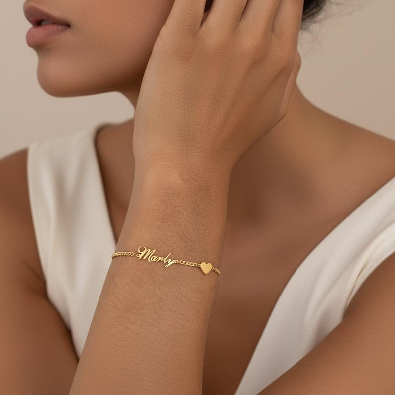 Gold bracelet with heart detail on a person's wrist against a neutral background