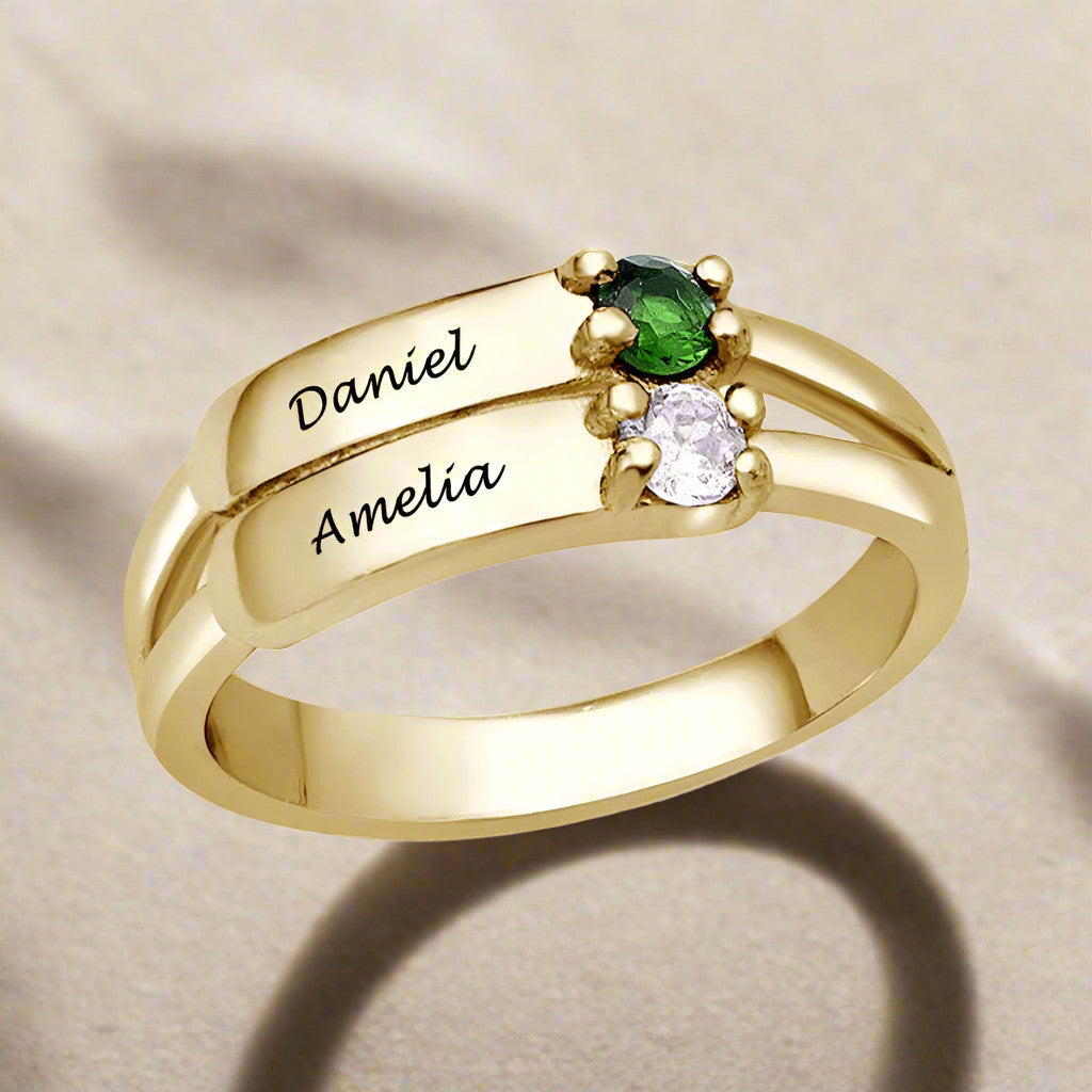 A gold-coloured silver ring featuring two engraved names and two gemstones.