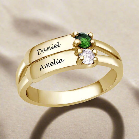 A gold-coloured silver ring featuring two engraved names and two gemstones.