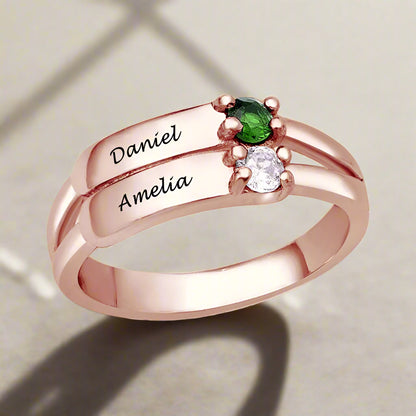 A rose gold-coloured silver ring featuring two engraved names and two gemstones.