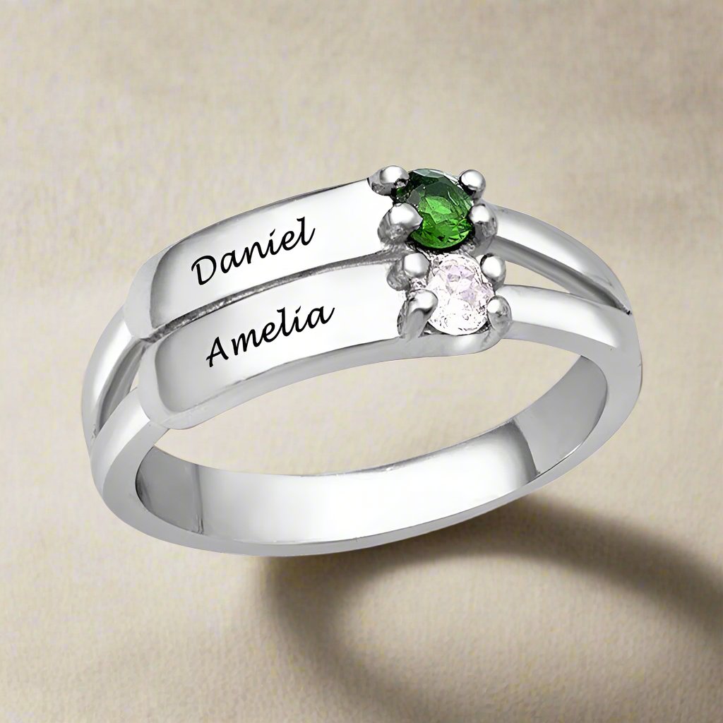 A silver-coloured ring featuring two engraved names and two gemstones.