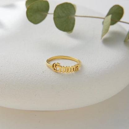 Gold ring with engraved text on a white surface with green leaves in the background