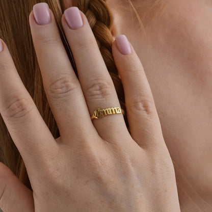 Close-up of a hand wearing a gold name ring with pink nail polish.