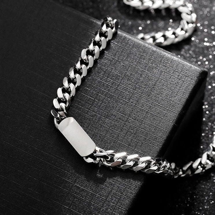 A silver-coloured, titanium steel necklace with a six-sided grinding NK chain design, displayed on a black box.