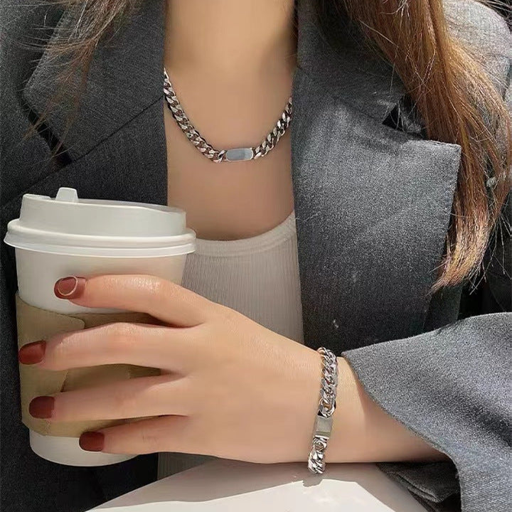 A person wearing a silver-coloured, titanium steel necklace and bracelet, both with a six-sided grinding NK chain design.